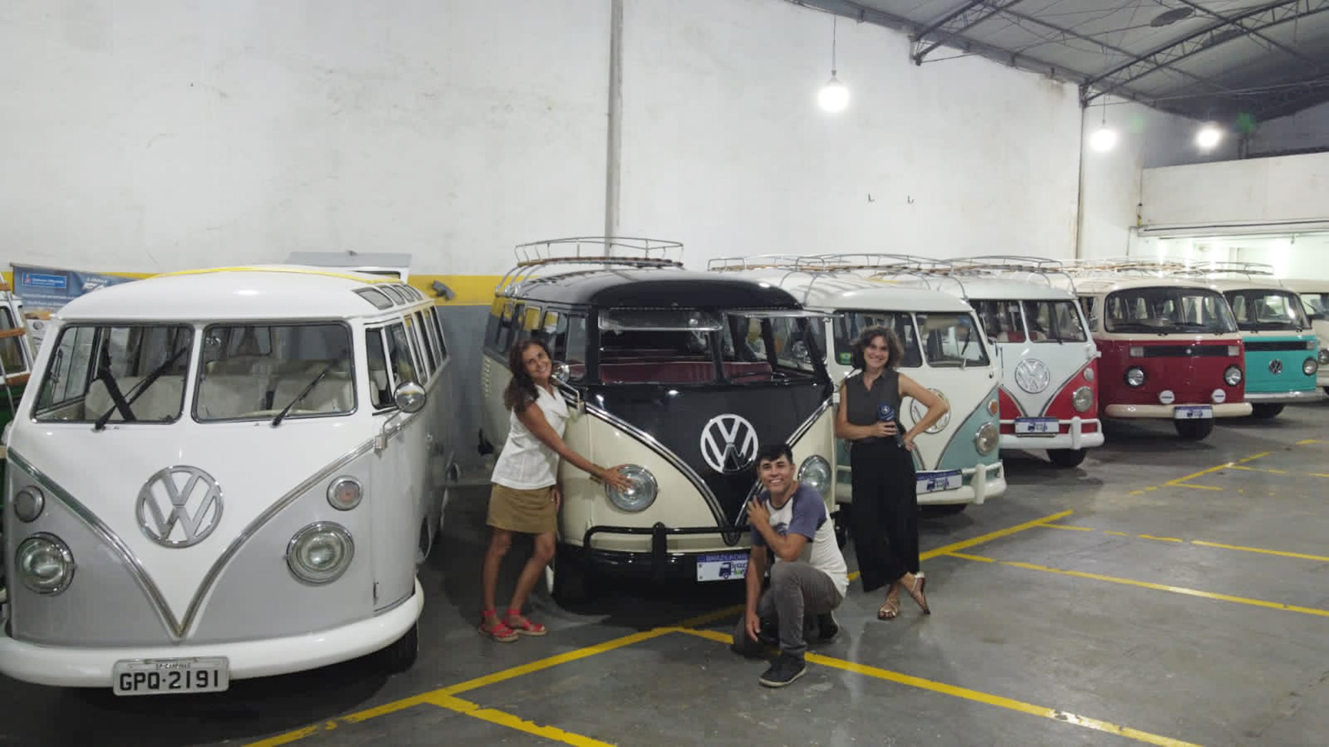 Mitarbeitende stehen vor alten restaurierten VW-Bussen in einer Halle. | ARD-Studio Rio