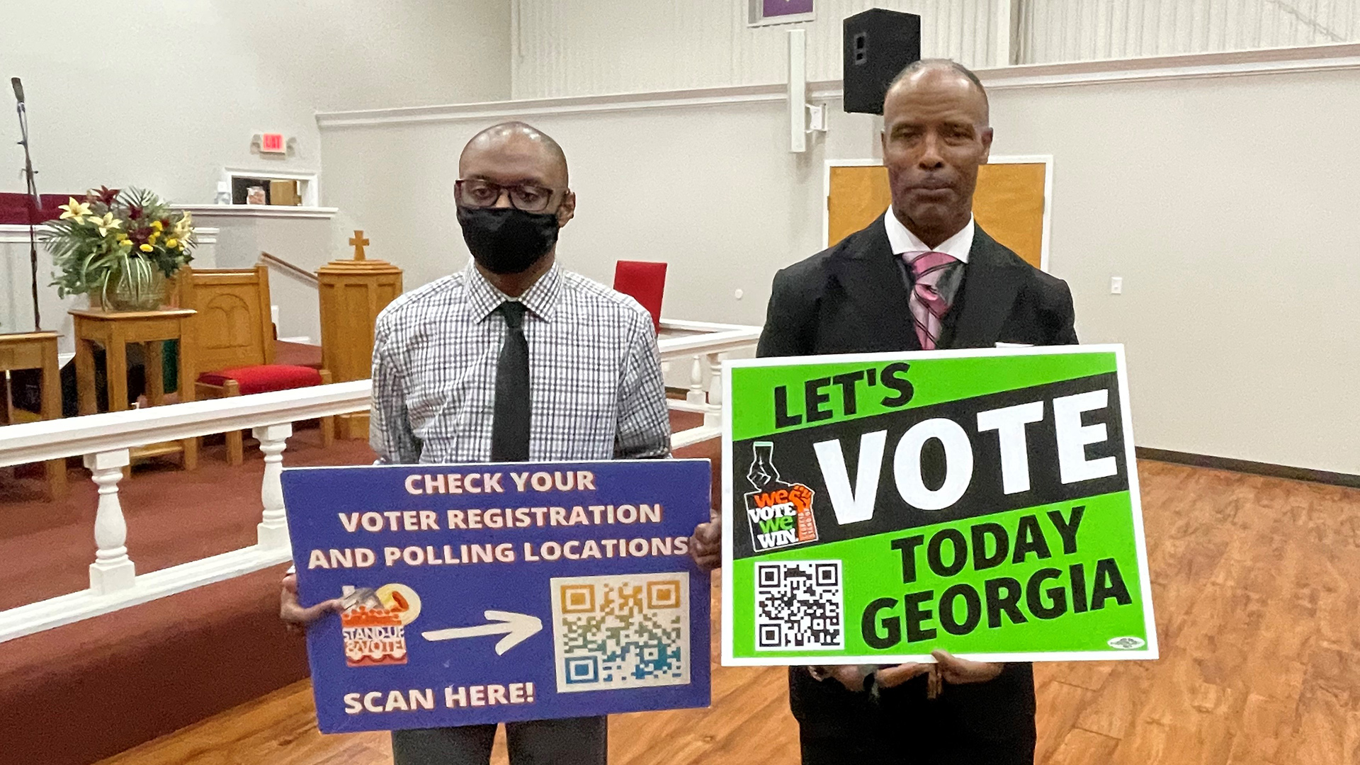 Zwei Schwarze Männer mit Schildern, auf denen Hinweise und QR-Codes zum Wählen in Georgia stehen. | Gudrun Engel