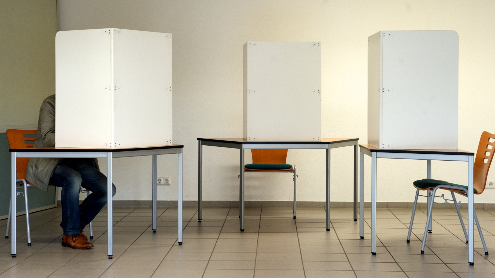 Ein einzelner Mann sitzt in einer von drei Wahlkabinen. | dpa