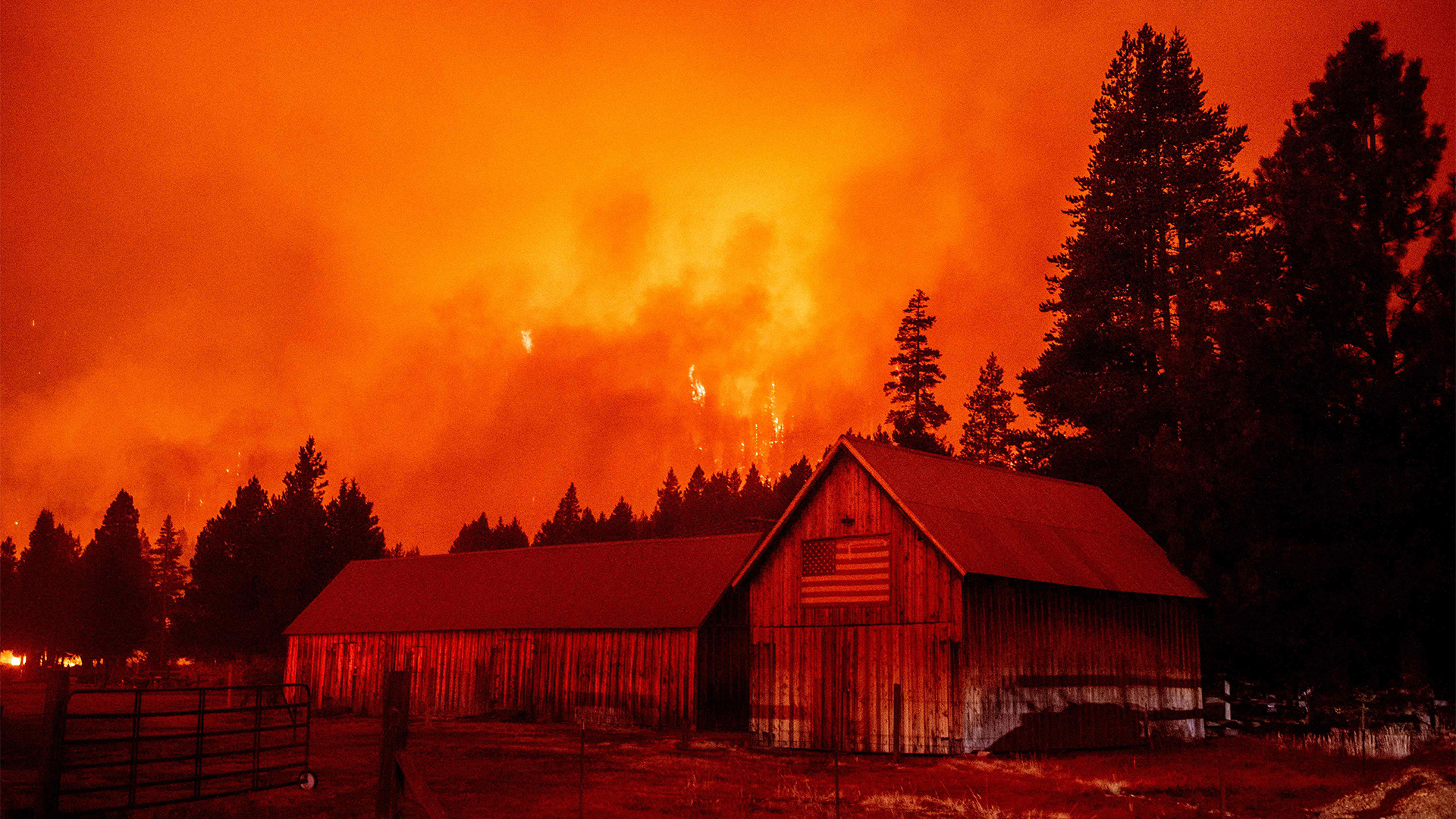 Flammen schlagen über einen Hang hinter einem Gebäude mit einer amerikanischen Flagge, in South Lake Tahoe, Kalifornien. | AFP