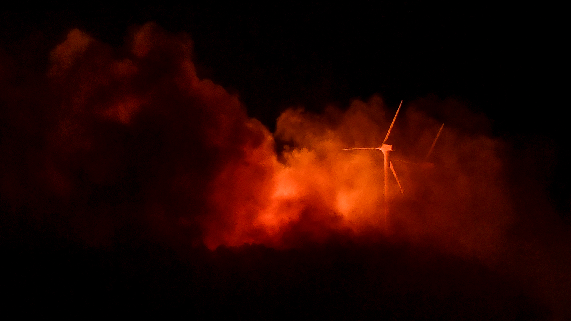 Das Feuer eines Waldbrandes beleuchtet Windräder. | AFP