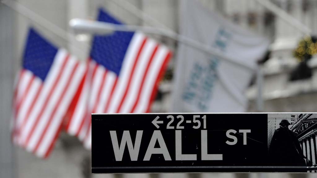 Ein Straßenschild der Wall Street in New York vor US-Flaggen.
