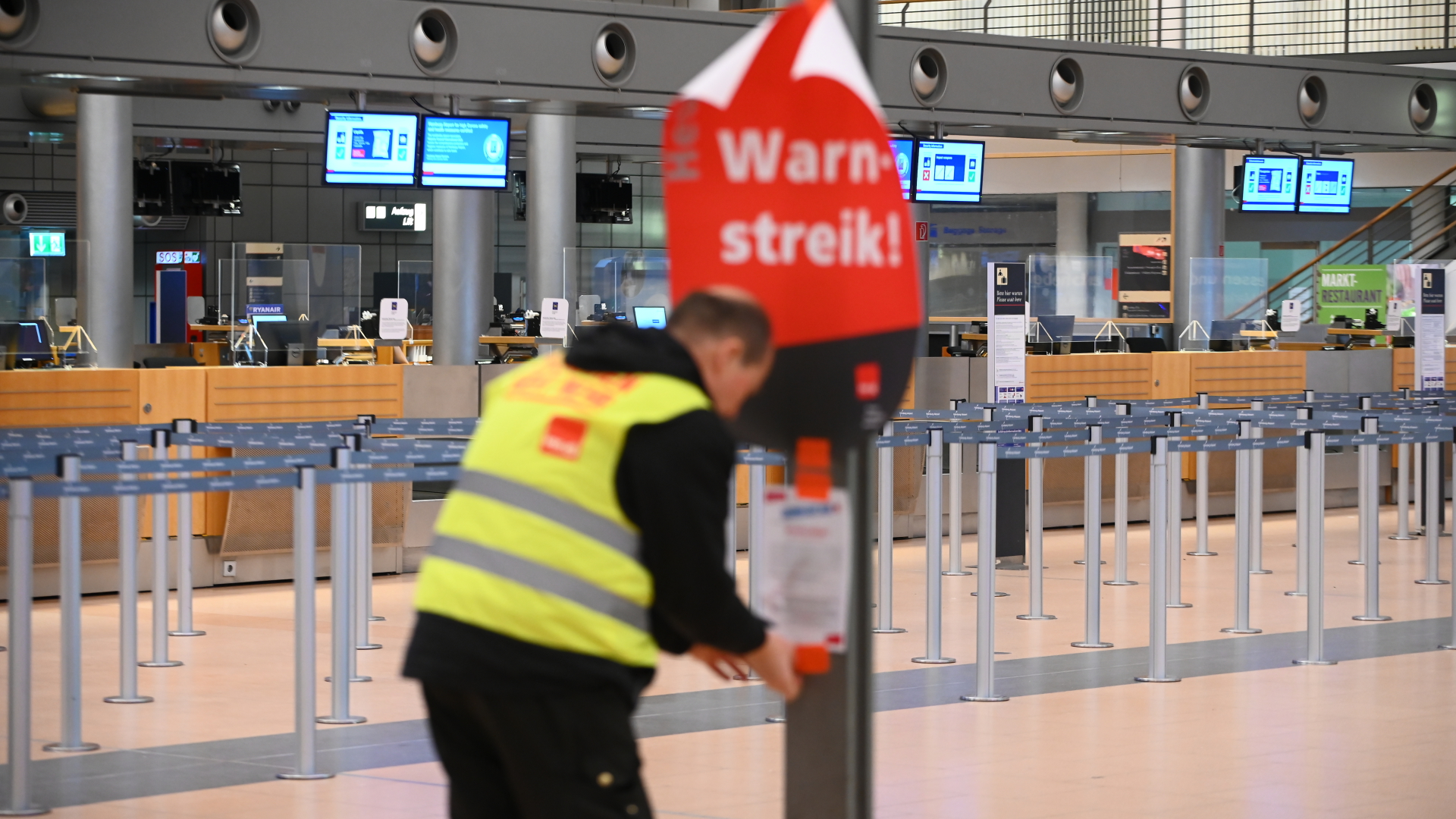 Ein Gewerkschaftsvertreter klebt ein Plakat mit der Aufschrift "Warnstreik!" und einen Flyer an die Anzeigetafel im leeren Terminal 2 am Hamburger Flughafen. | dpa
