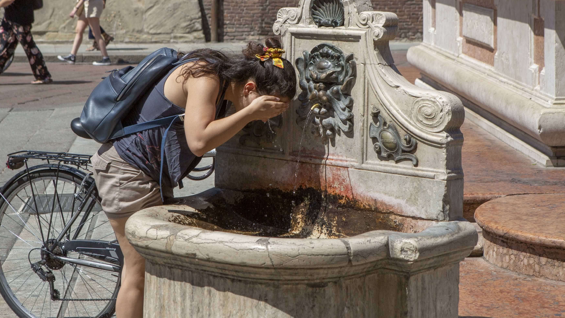 Eine Frau erfrischt sich an einem Brunnen in Bologna