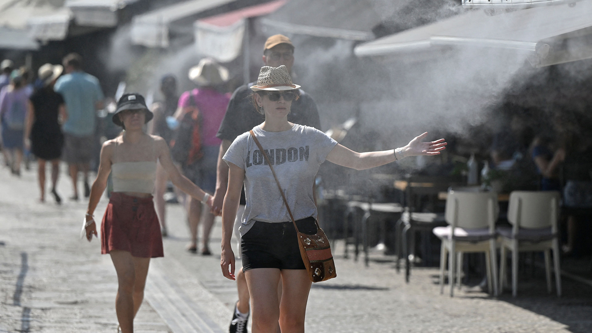 Touristen laufen während der Hitzewelle in Athen an einem Café durch Wasserstrahlen, das auf den Gehweg versprüht wird. | AFP