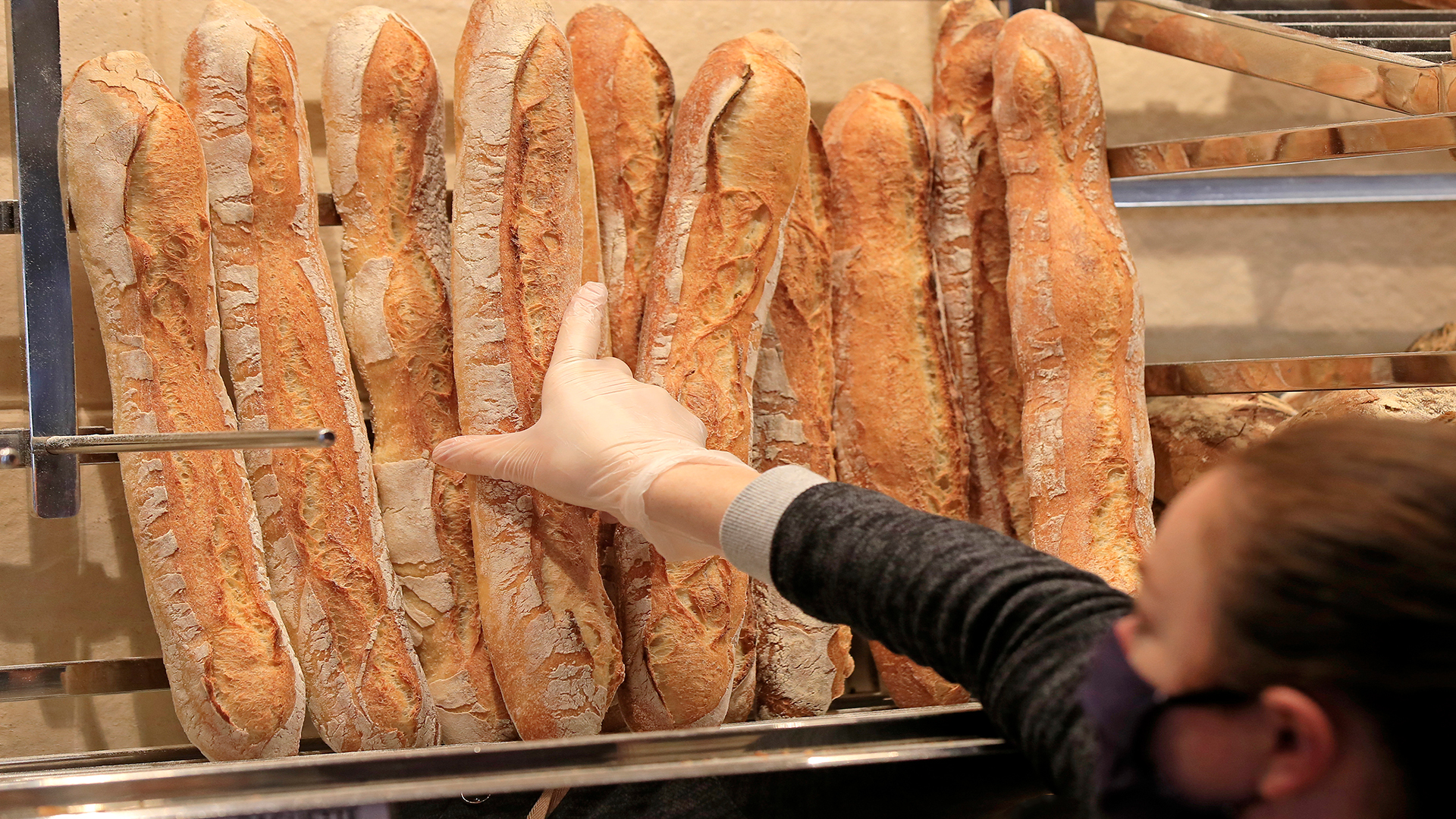 Ein Verkäuferin mit Mundschutz nimmt ein Baguette in einer Bäckerei in Paris. | Stefanie Markert