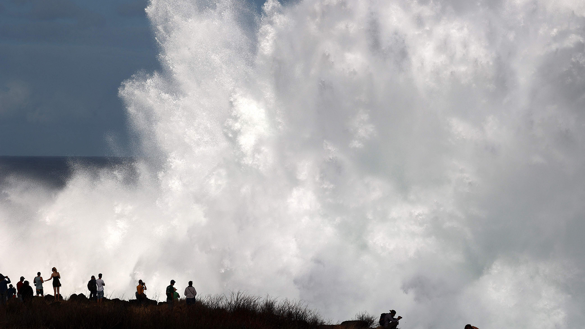 Menschen vor einer großen sich brechenden Welle. | AFP