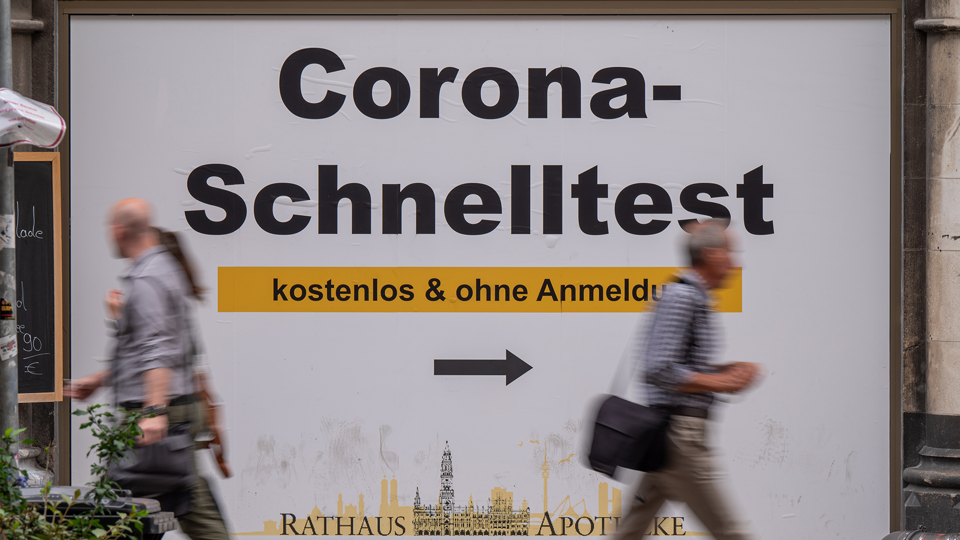 Passanten gehen an einem Plakat mit der Aufschrift "Corona-Schnelltest - kostenlos und ohne Anmeldung" vorbei. | dpa