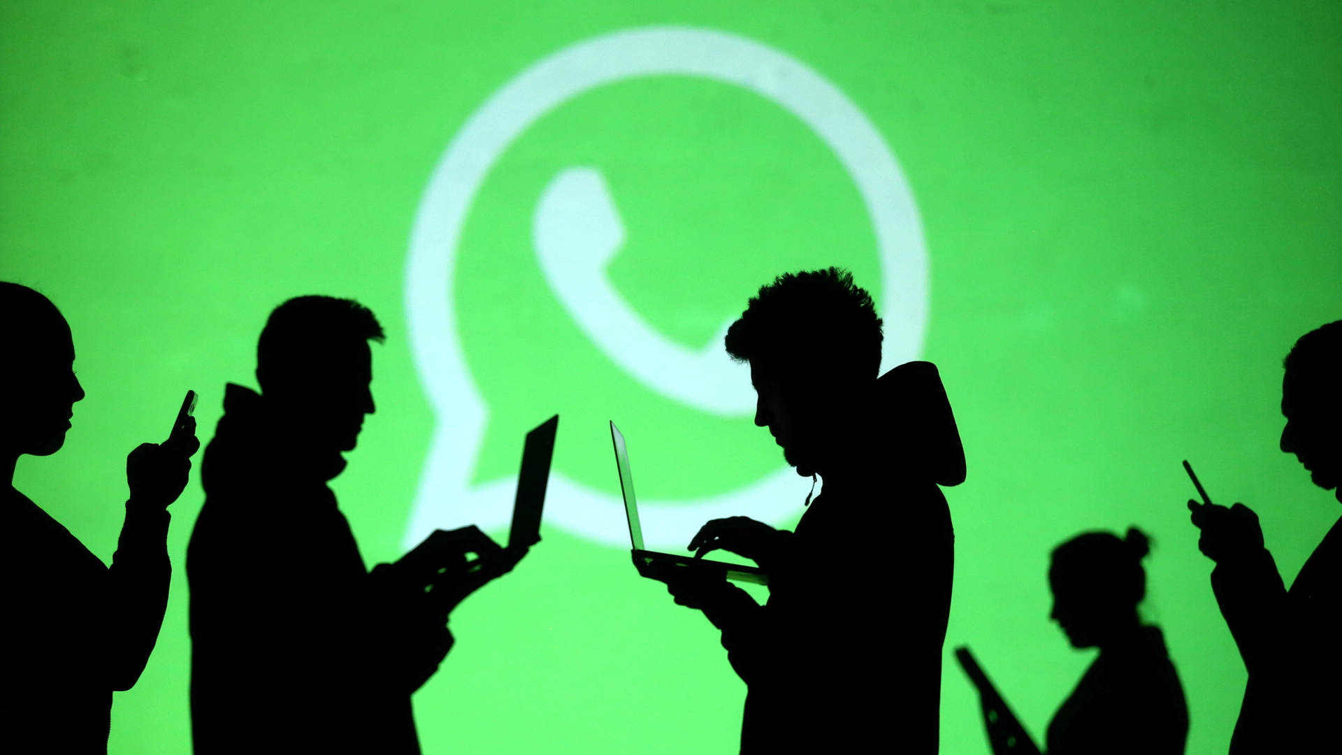 Silhouetten von Menschen mit Laptops und Smartphones in der Hand, im Hintergrund ein großes Whatsapp-Logo (Weißer Kreis mit Telefon-Symbol in der Mitte) | REUTERS