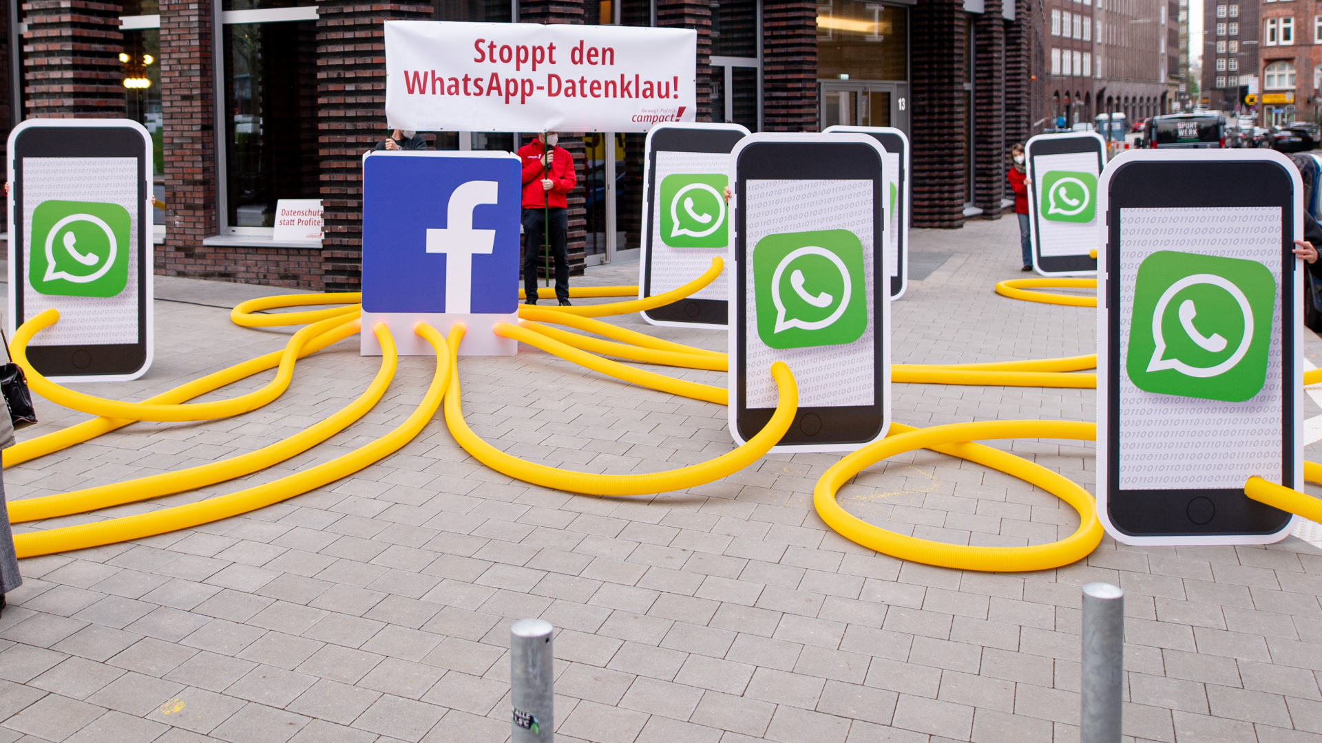 Modelle von Smartphones mit großen WhatsApp-Logos sind bei einer Protestaktion auf einer Straße aufgebaut | dpa