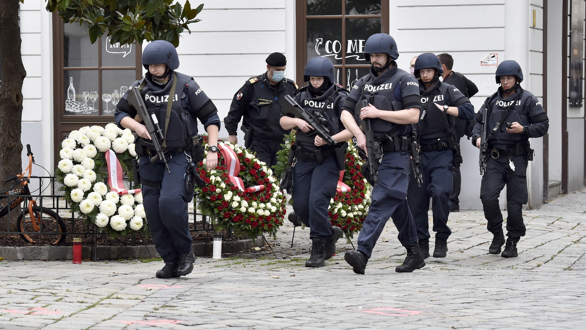 Polizisten gehen nach dem Terroranschlag an Blumenkränzen nahe des Tatorts in Wien vorbei. | dpa