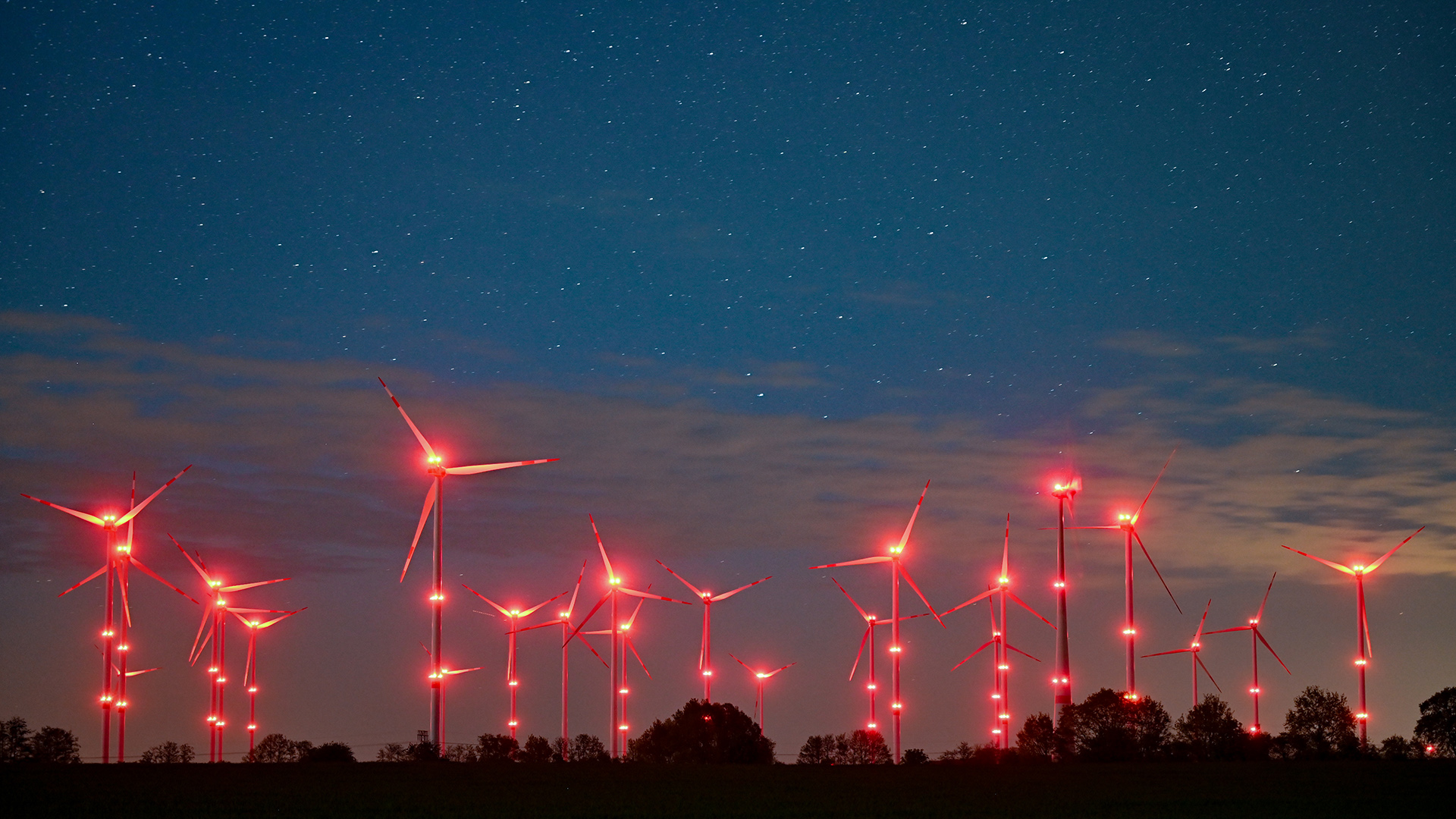 Die roten Positionslichter an Windenergieanlagen in Jacobsdorf in Brandenburg erhellen den Nachthimmel und die Landschaft.