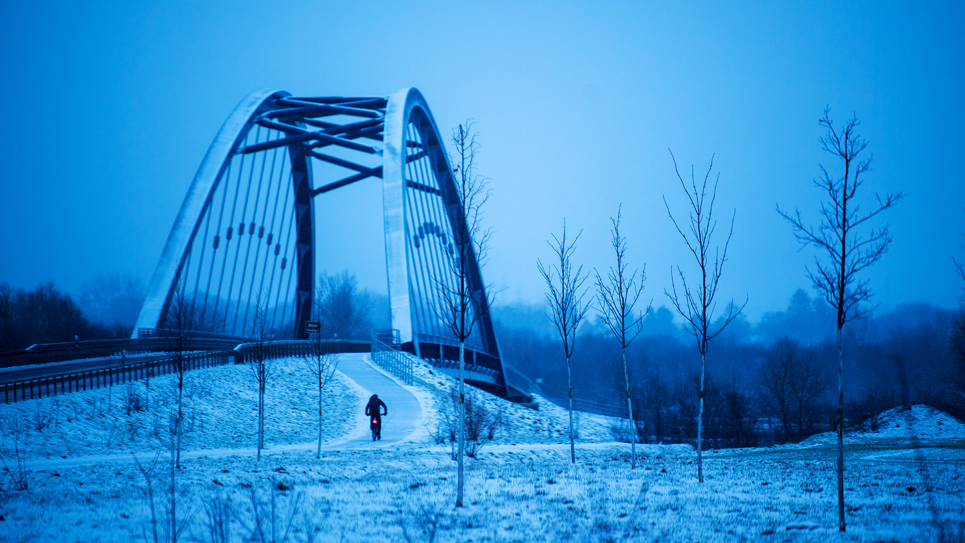 Ein Radfahrer fährt einen winterlich verschneiten Radweg entlang.  | dpa