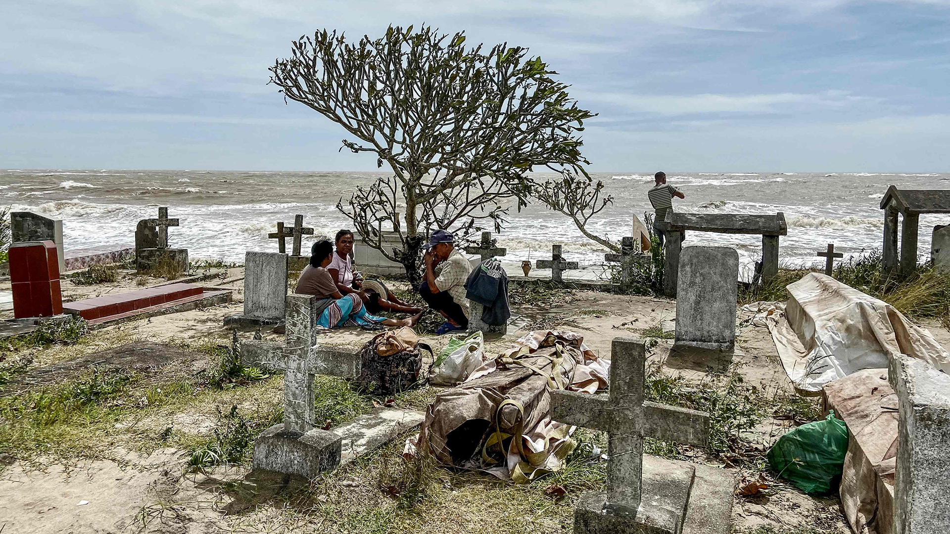 Angehörige sitzen neben zerstörten Gräbern auf dem örtlichen Friedhof in Mahanoro, Madagaskar. | AFP