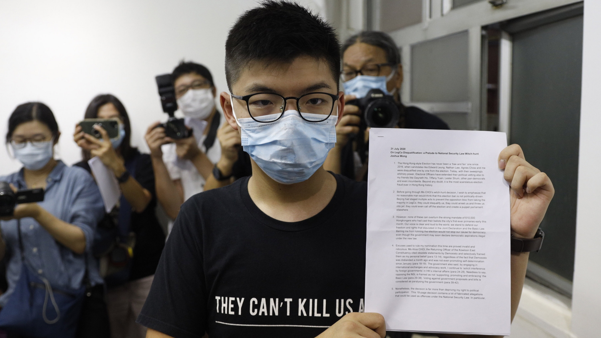Der Hongkonger Aktivist Joshua Wong hält ein Protestschreiben während einer Pressekonferenz in die Kamera. | AP