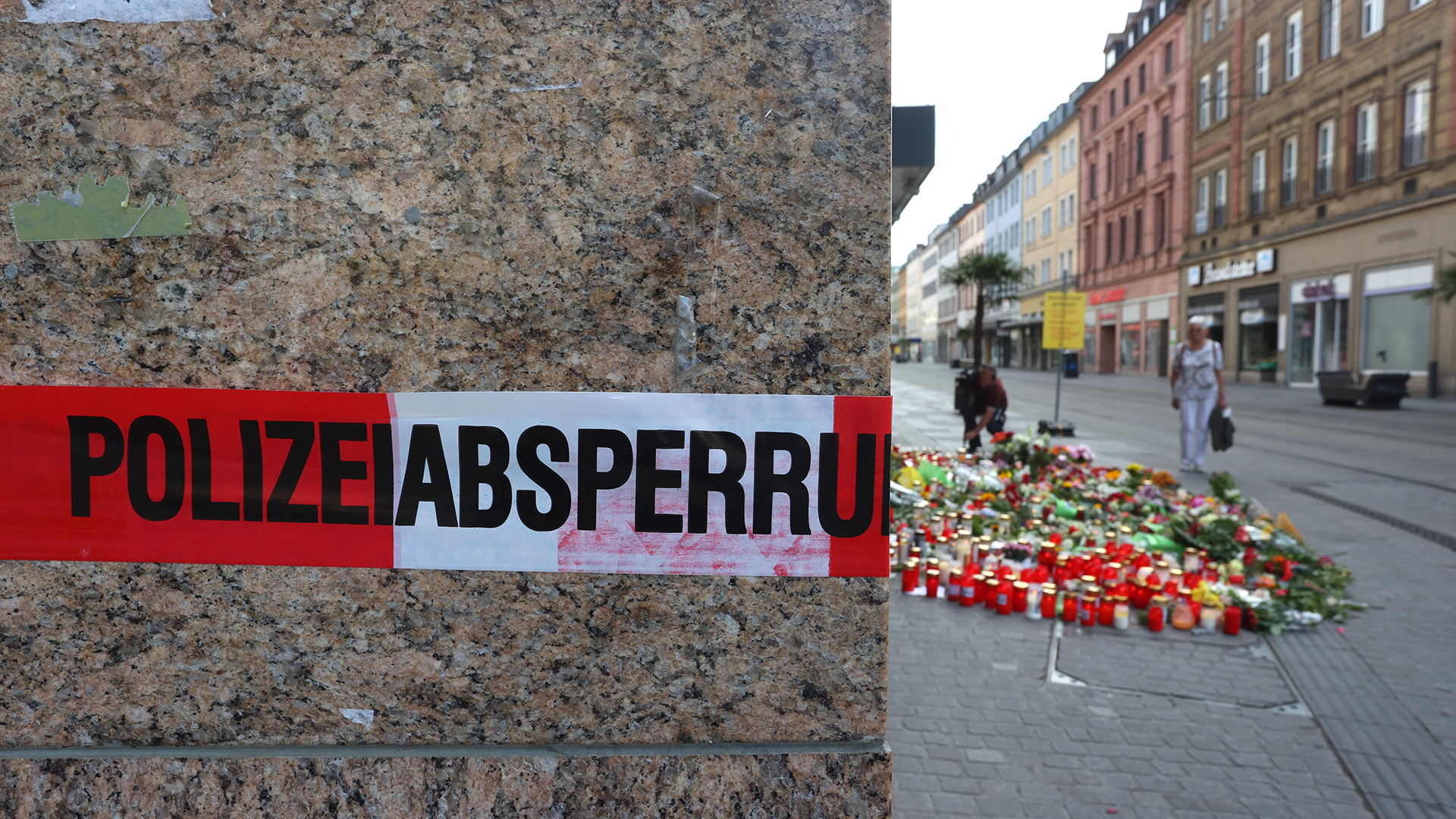 Blumen und Kerzen liegen am Tatort vor dem abgesperrten Kaufhaus in Würzburg. | dpa
