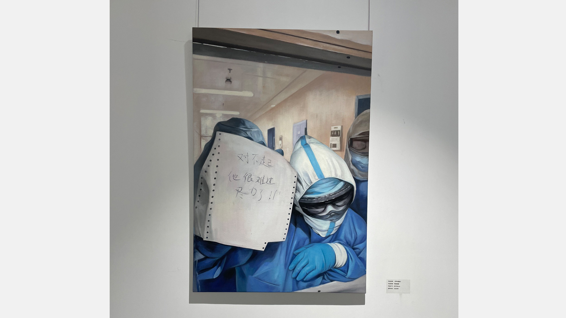 Das Foto von Menschen in Schutzanzügen, die ein Blatt Papier an eine Scheibe halten, hängt an einer Wand. | Eva Lamby-Schmitt