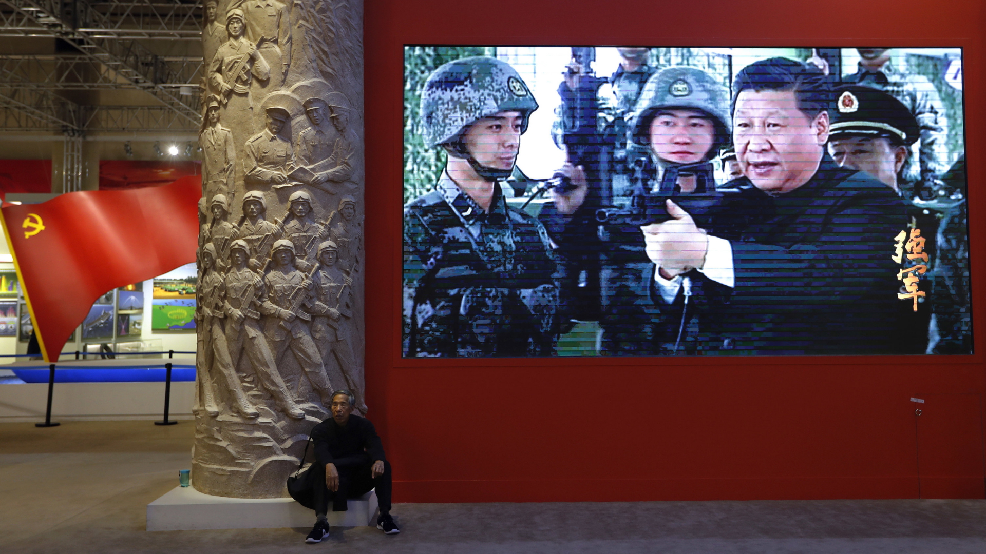 Chinas Staatschef Xi Jinping posiert vor Soldaten mit einer Waffe - Propagandafilm in einer Ausstellungshalle in Peking. | AP