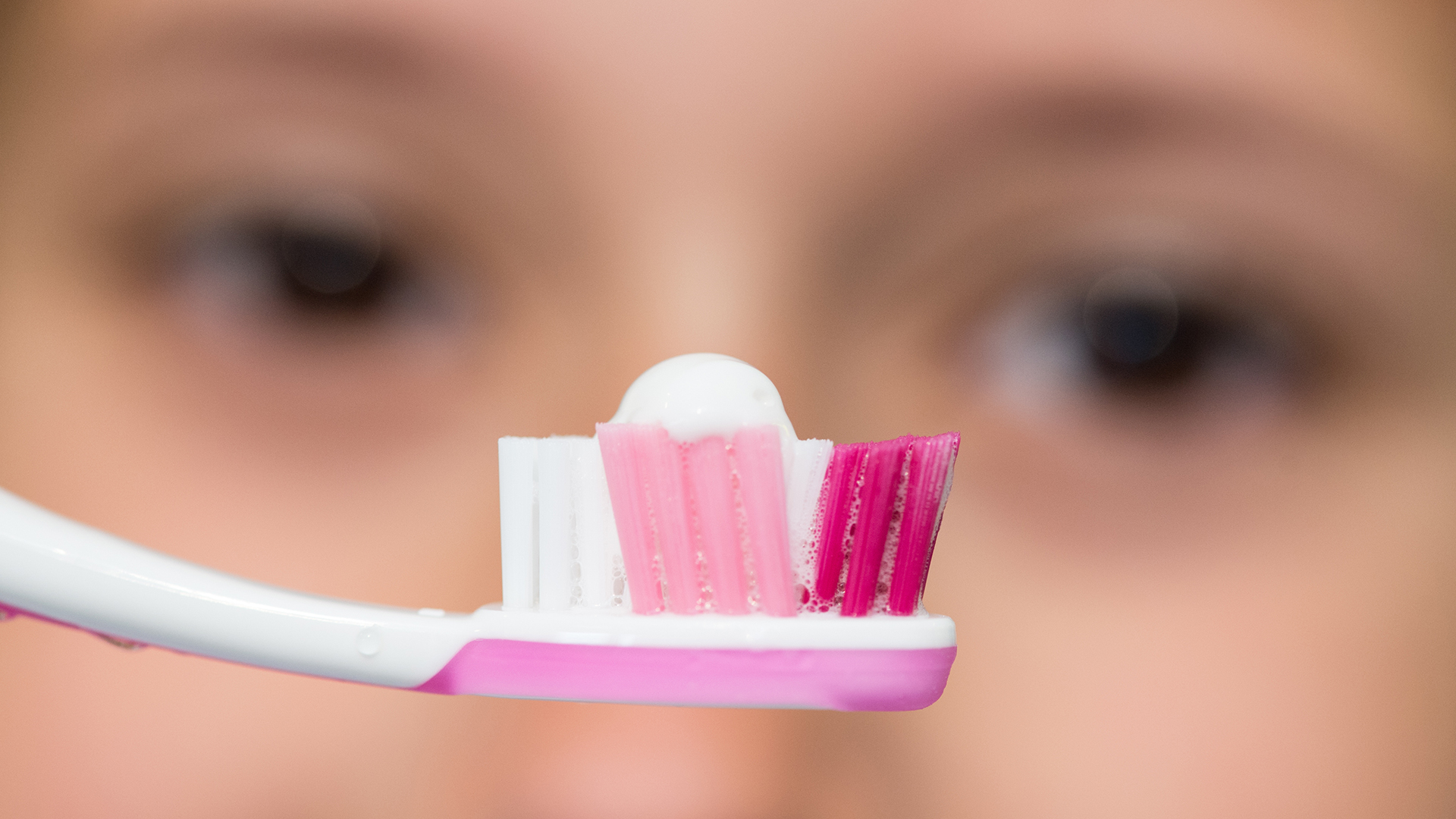 Ein Mädchen schaut ihre Zahnbürste mit Zahnpasta an.  | picture alliance/dpa