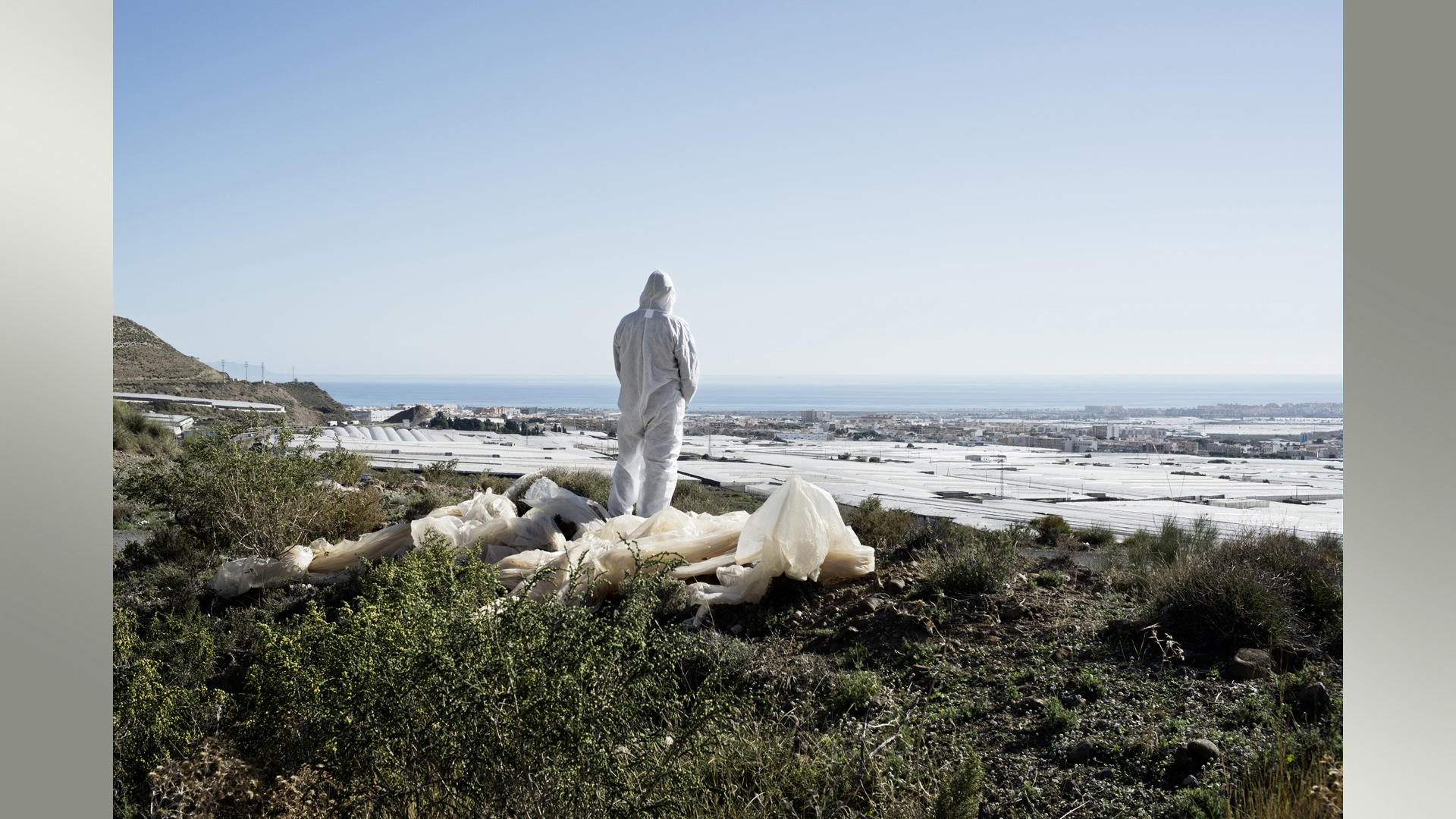 Eine Figur in einem Schutzanzug schaut auf mit Folie bedeckte Gemüseplantage in Südspanien | Raul Walch