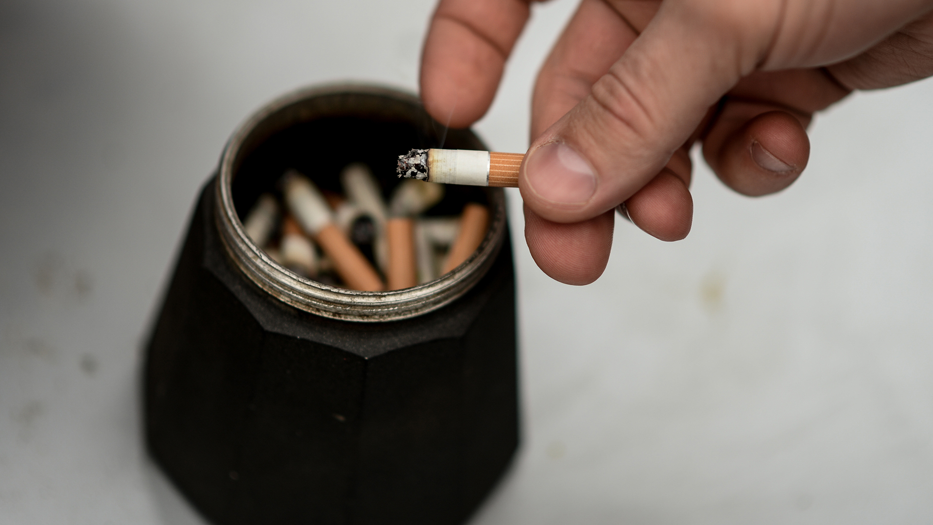 Ein Mann klopft die Asche einer Zigarette über einem Aschenbecher ab.