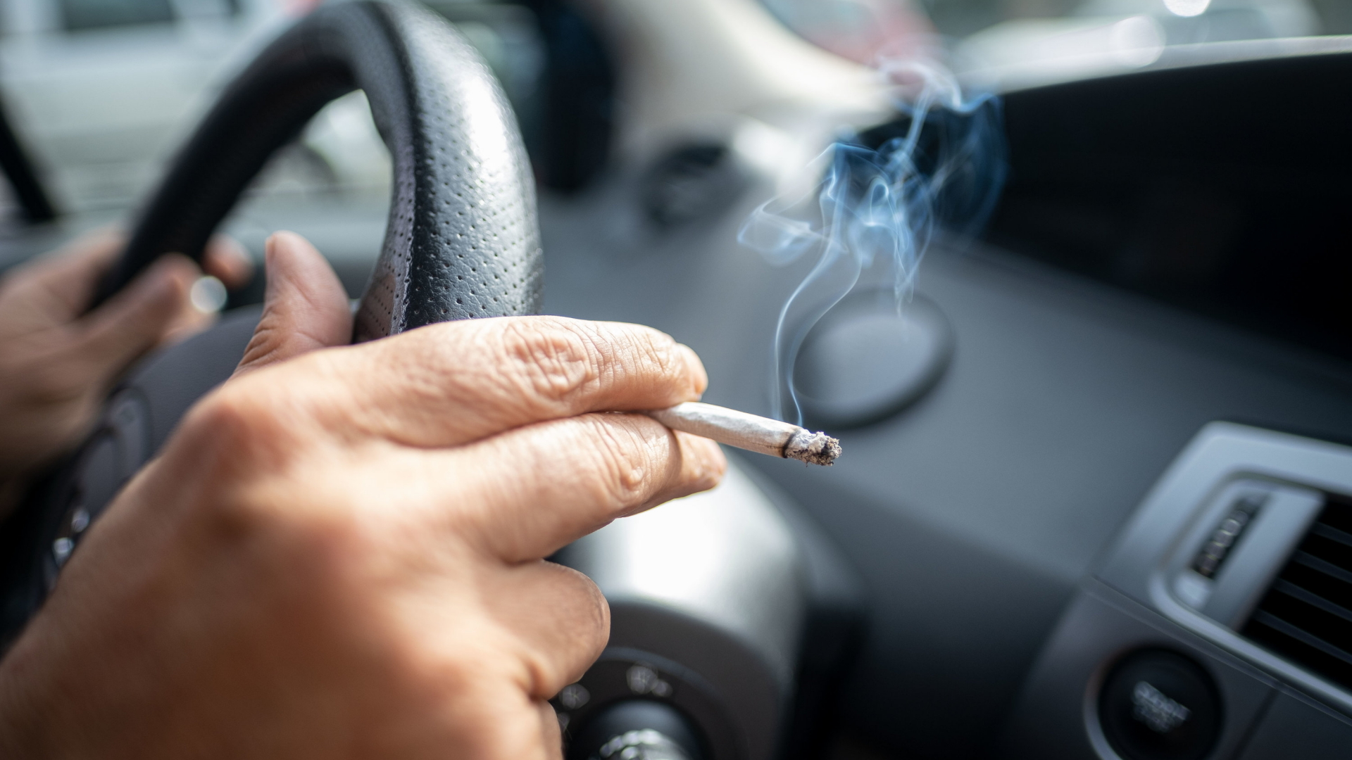Eine Person am Steuer eines Autos hält eine Zigarette in der Hand.