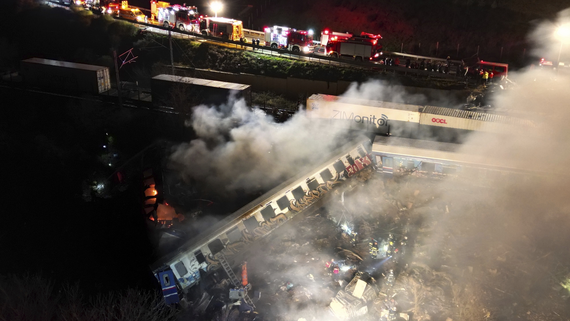 Rauch steigt auf, während Feuerwehrleute und Rettungskräfte nach einem Zusammenstoß zweier Züge in der Nähe von Larissa (Griechenland) im Einsatz sind. | dpa