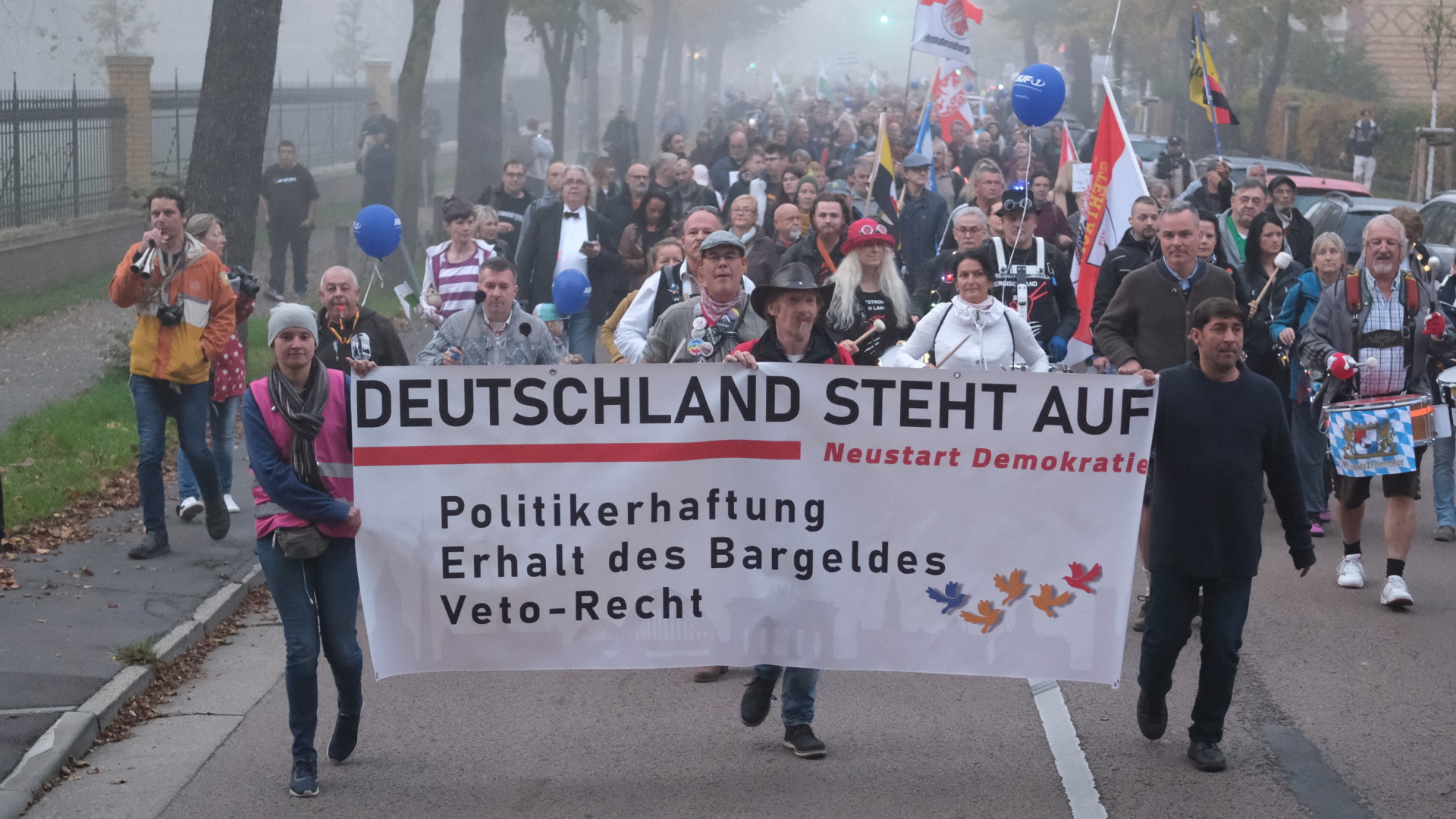 Teilnehmer einer Demonstration gehen mit einem Transparent und Fahnen eine Straße in Lutherstadt Wittenberg in Sachsen-Anhalt entlang. | dpa