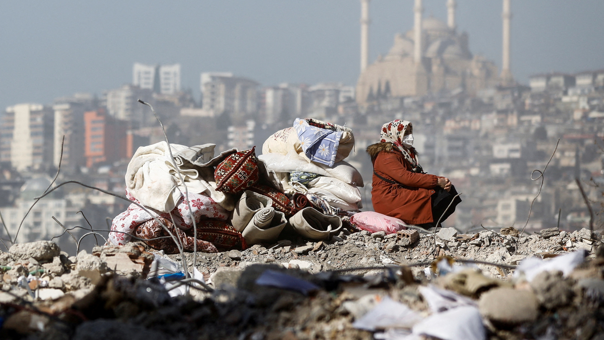 Eine Frau sitzt mit wenigen Habseligkeiten auf den Trümmern kaputter Gebäude in der Türkei.