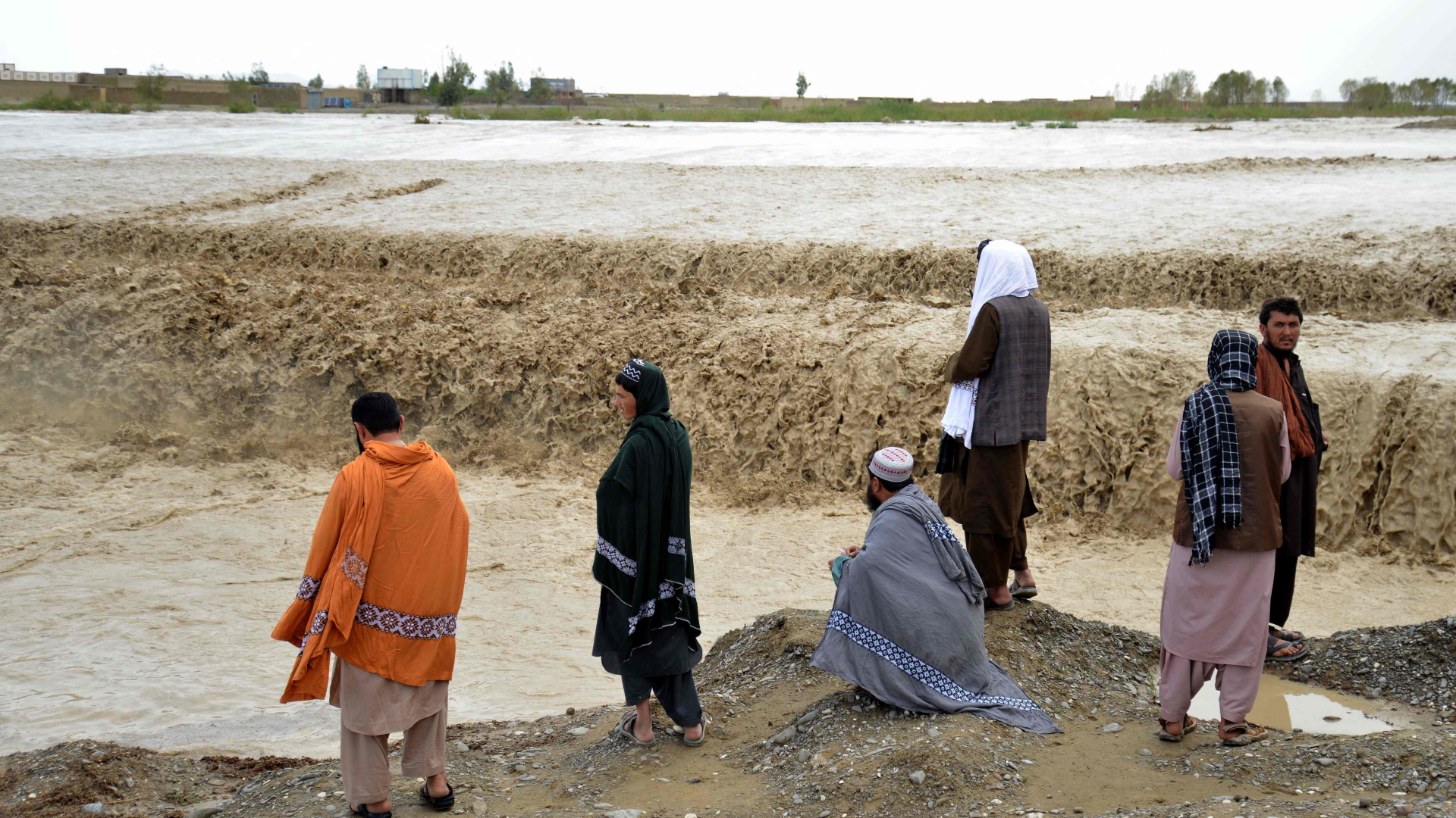 Menschen in Afghanistan stehen vor einem Wasserfall. Das Wasser ist braun und voller Sedimente.