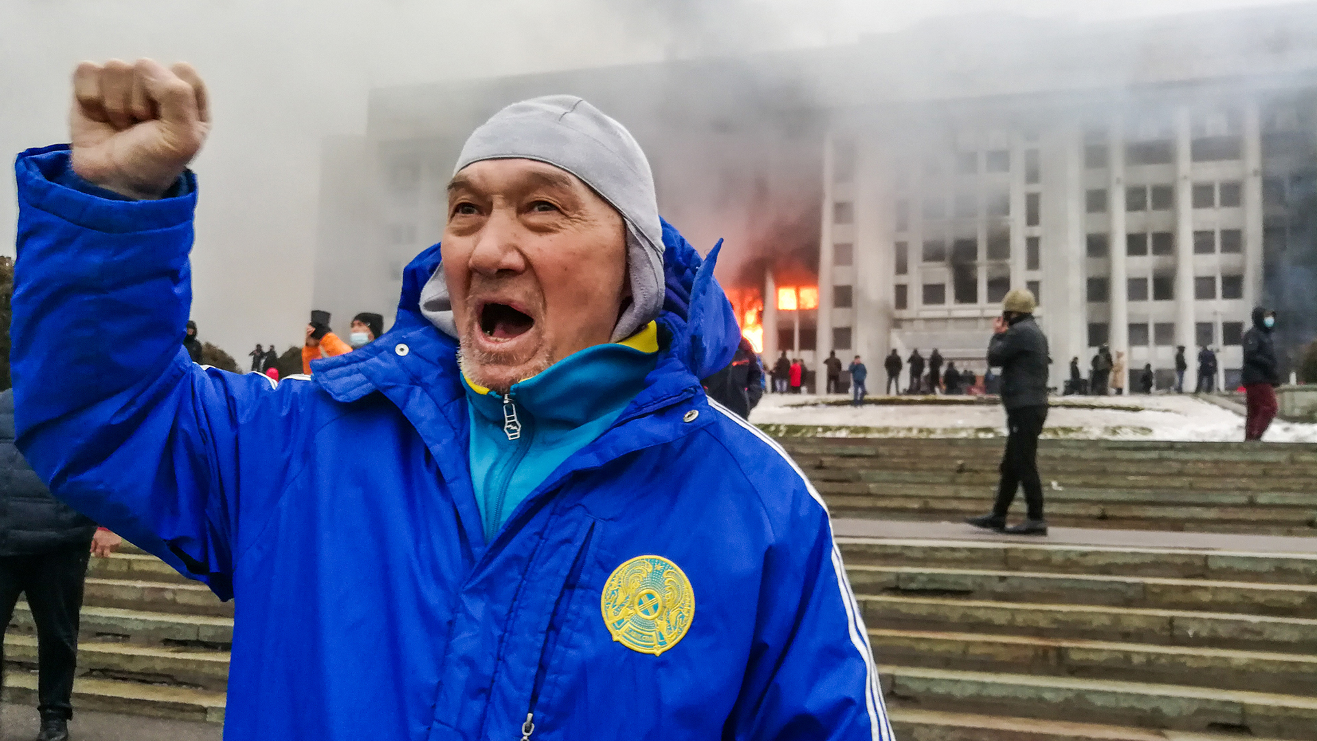 Ein Mann demonstriert vor dem brennenden Büro des Bürgermeisters in Almaty. | picture alliance/dpa/TASS