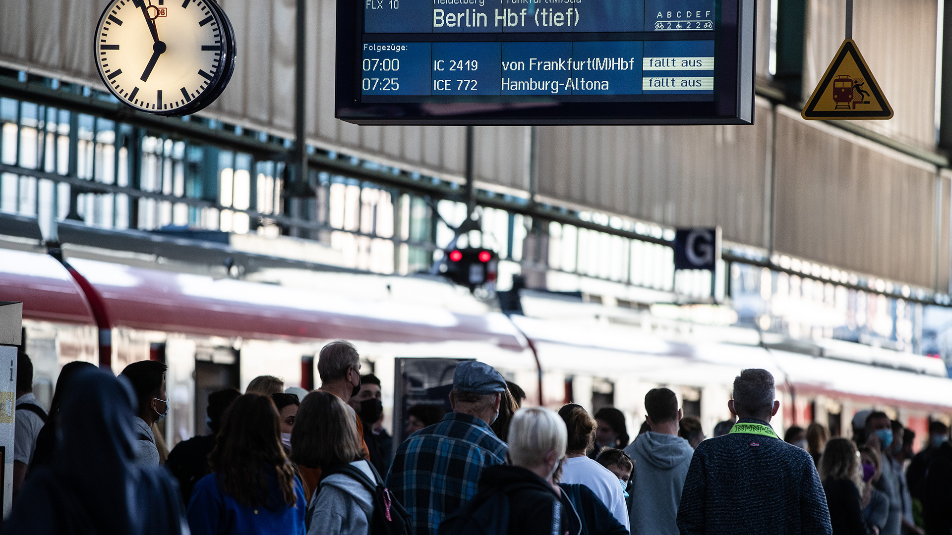 Fahrgäste mit Koffern stehen vor einer Anzeigetafel der Bahn. | null