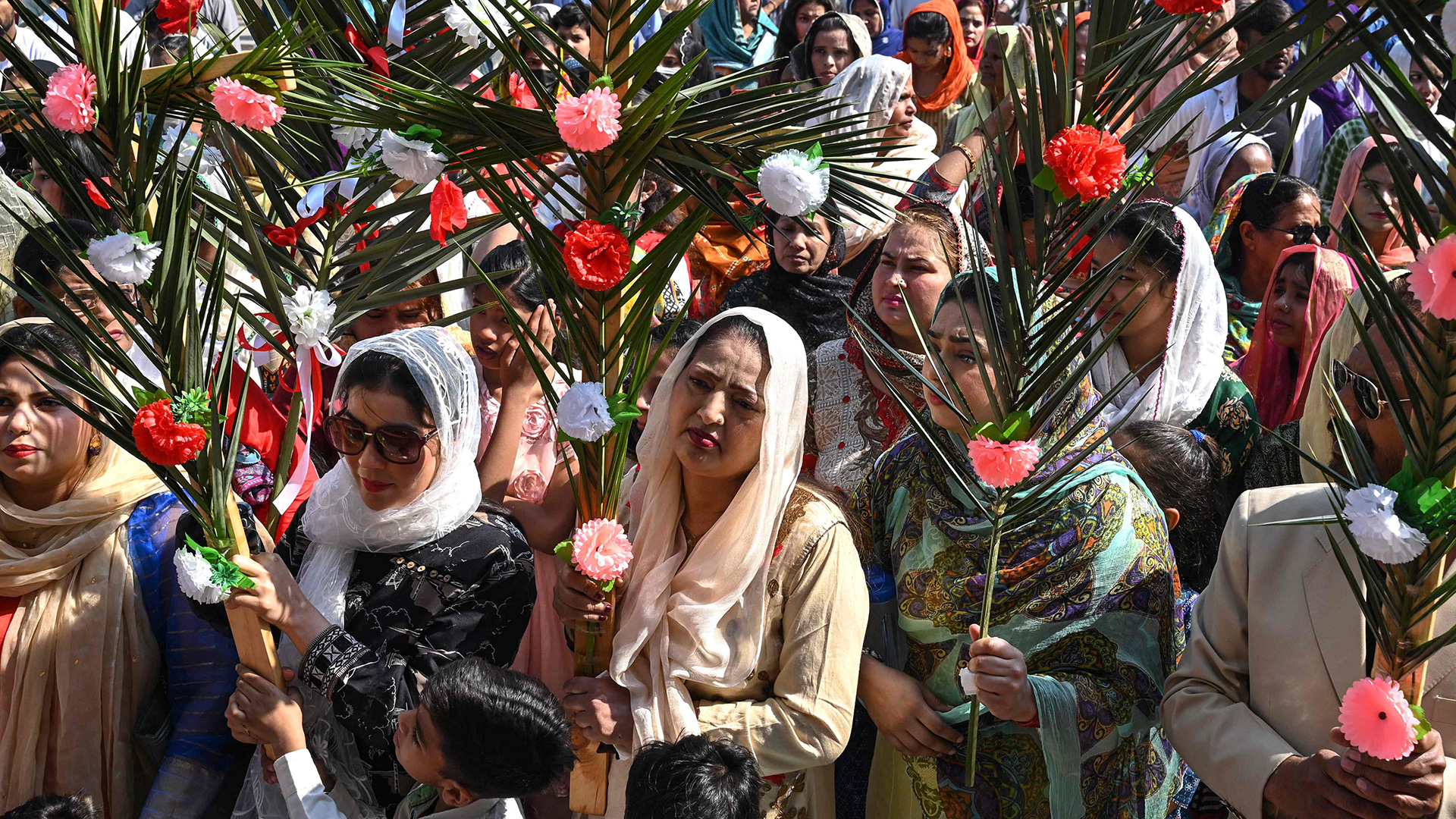 Menschen halten mit Blumen geschmückte Palmzweige in den Händen. | AFP