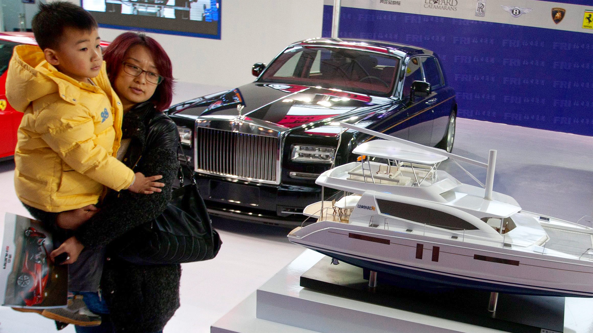 Chinesische Kundin mit Kind begutachtet einen Rolls Royce und das Modell einer Luxusjacht | picture alliance / dpa