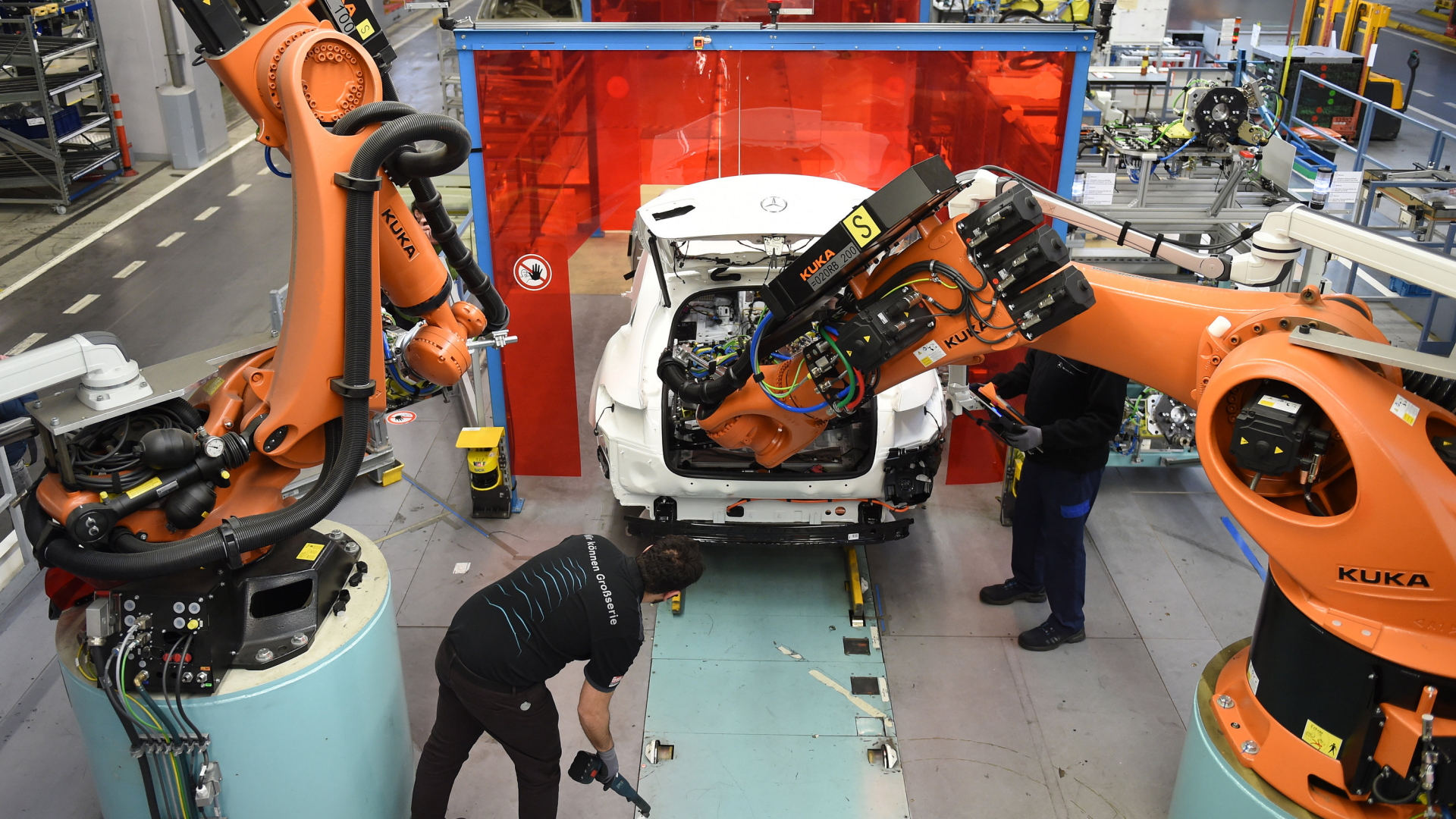 Mitarbeiter von Mercedes-Benz überwachen im Werk in Bremen, wie ein Roboter in das C-Klasse Hybrid Modell eine Batterie einsetzt. | dpa
