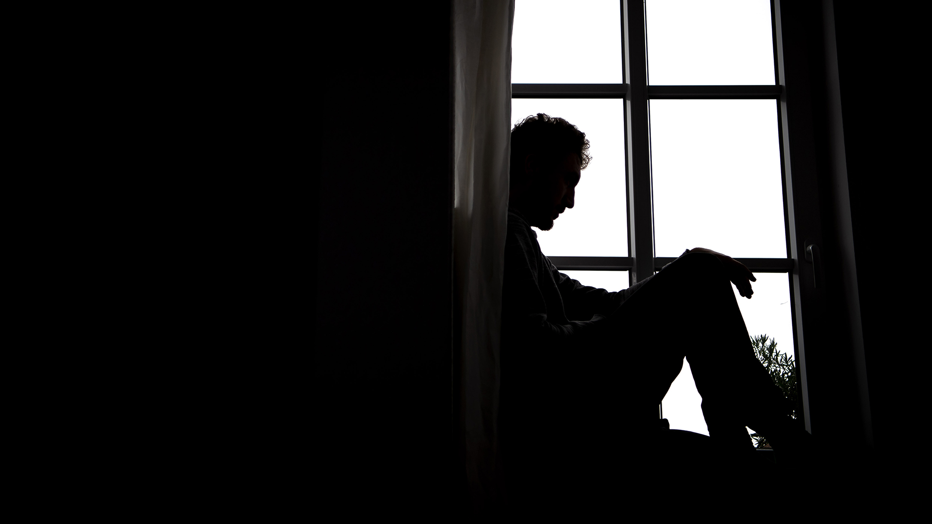 Ein Mann sitzt vor einem Fenster. 