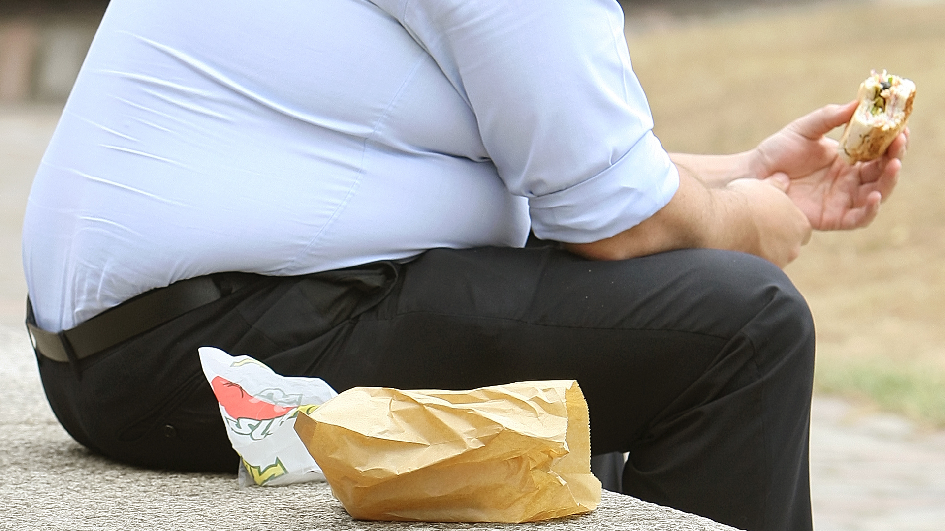 Ein übergewichtiger Mann isst ein belegtes Brot. | picture alliance / empics