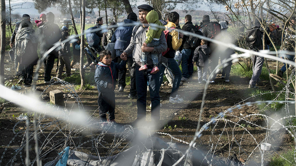 Flüchtlinge stehen an der griechisch-mazedonischen Grenze vor einem Grenzzaun