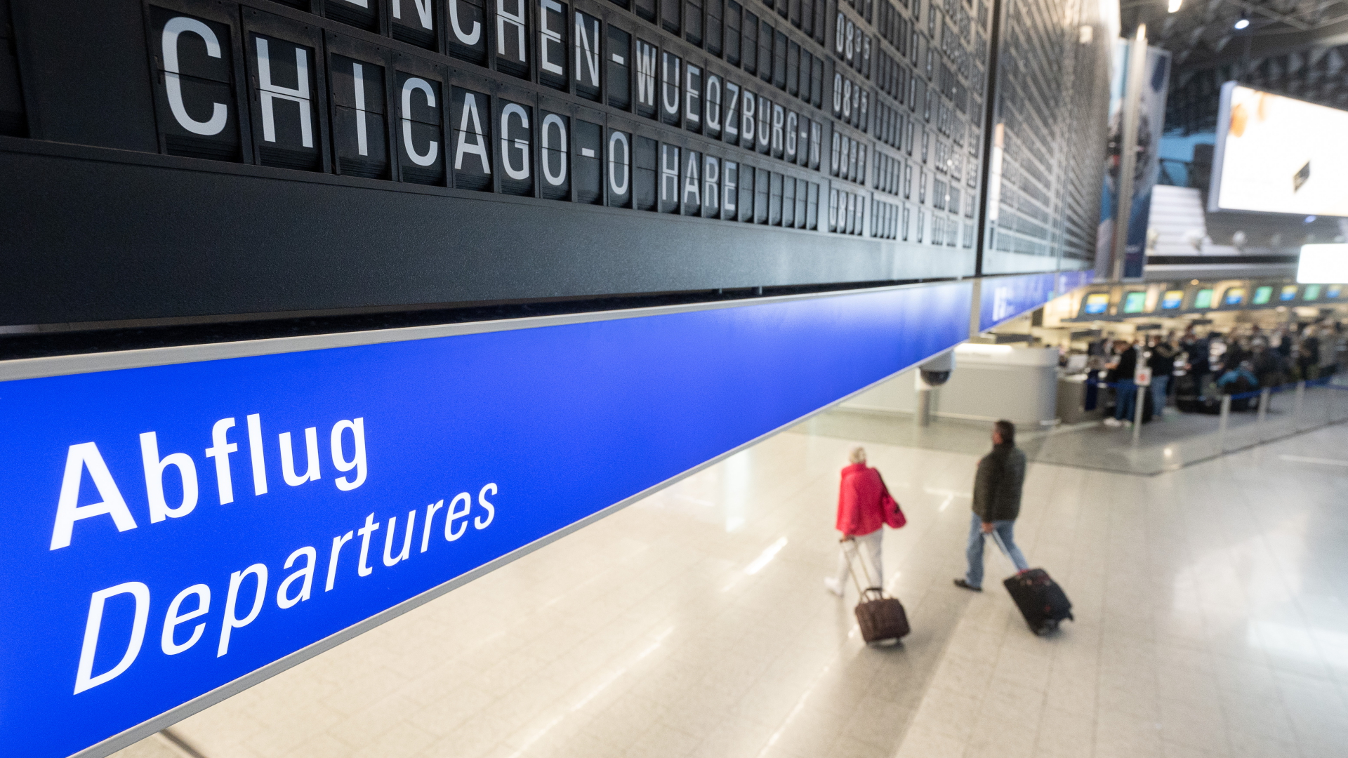 Ein Flug nach Chicago O'Hare in den USA wird auf dem Flughafen Frankfurt auf einer Tafel angezeigt unter der Passagiere mit Koffern entlang gehen. | dpa