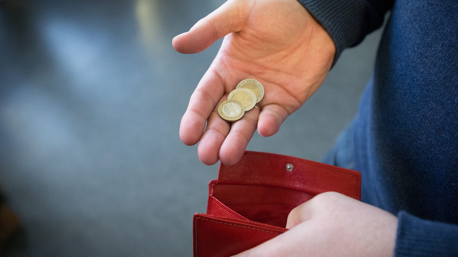 Münzen im Wert von fünf Euro werden über ein rotes Portemonnaie gehalten. | dpa