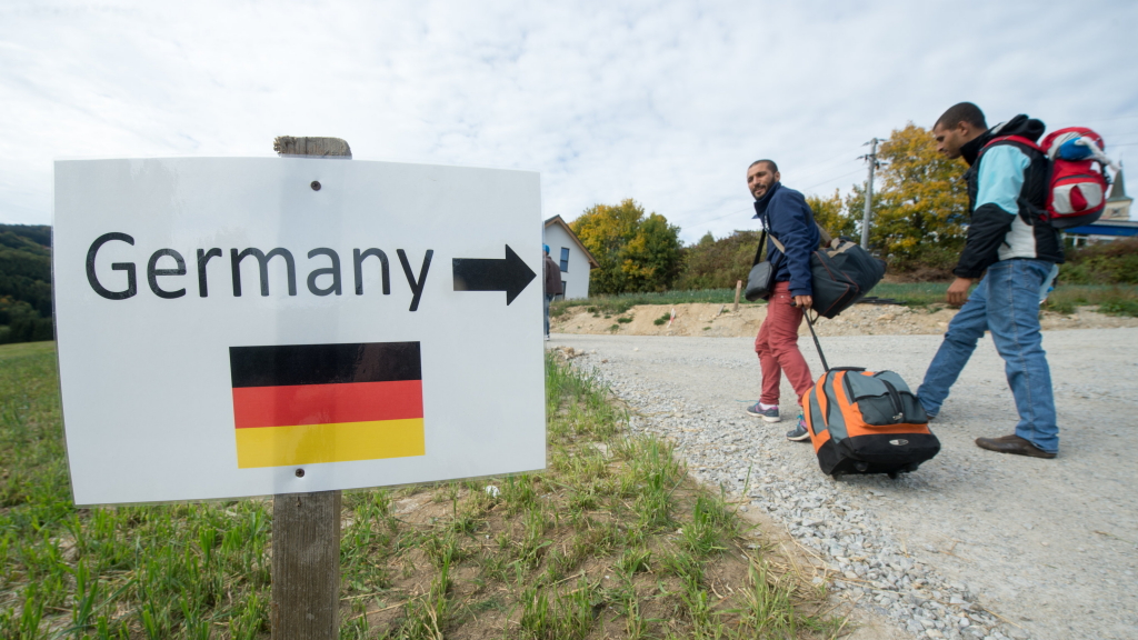 Flüchtlinge aus Syrien gehen am 06.10.2015 im österreichischen Julbach nahe der deutschen Grenze an einem Schild mit der Aufschrift "Germany" und der Abbildung einer deutschen Flagge vorbei