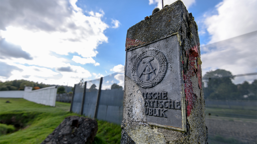 An einem ehemaligen Grenzstein in Mödlareuth (Thüringen) ist ein halb abgebrochenes Emblem der Deutschen Demokratischen Republik (DDR) zu sehen.  | dpa