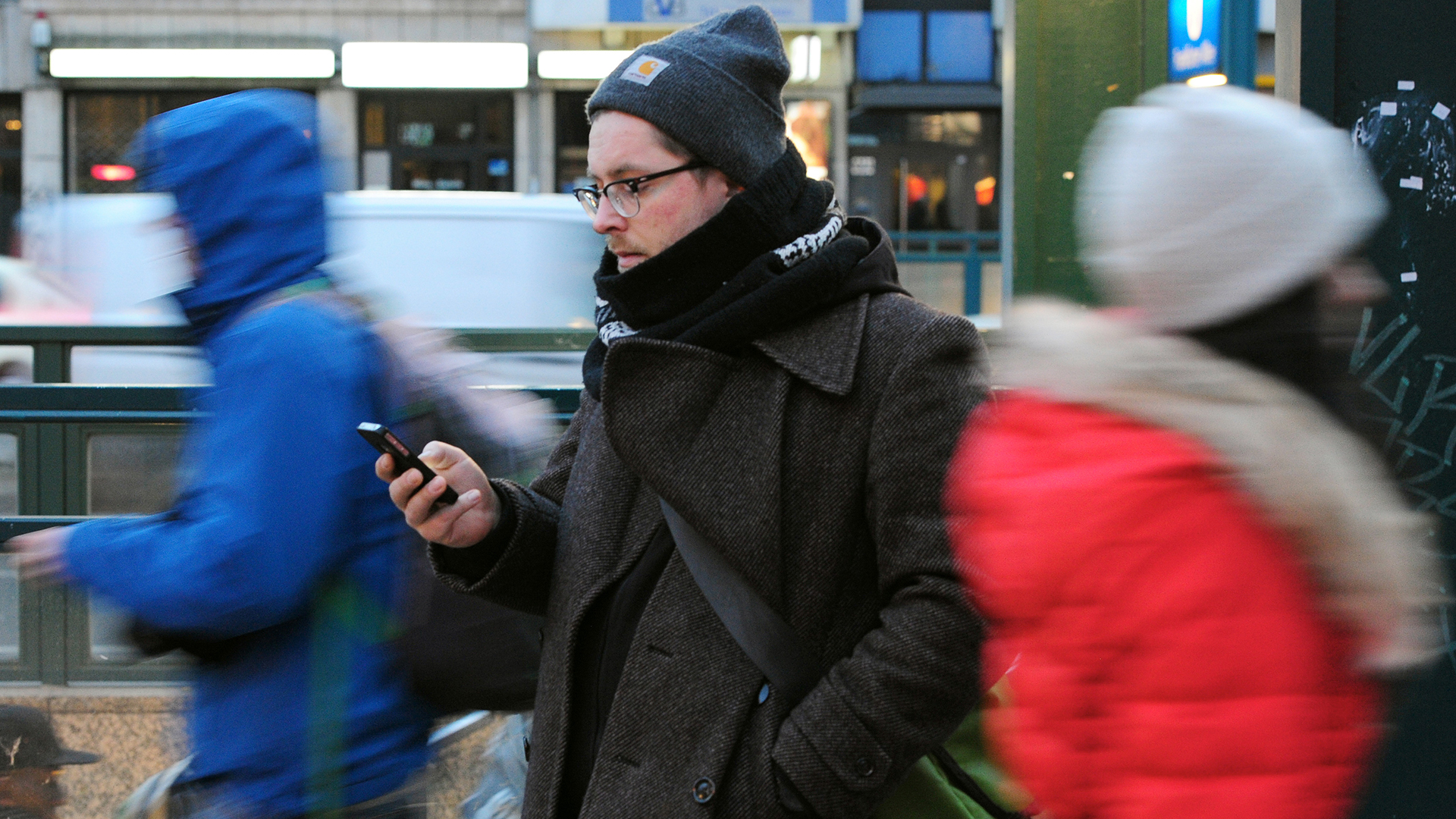 Ein junger Mann mit dem Blick auf sein Smartphone gerichtet an einer Straße in Berlin | picture alliance / dpa