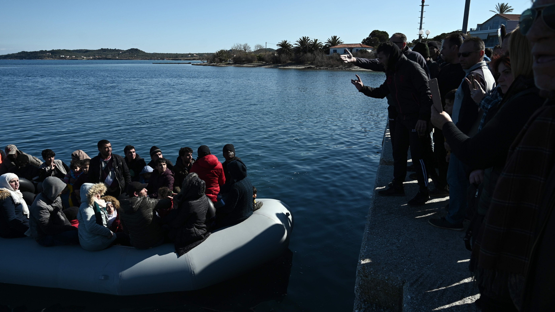 Migranten in einem Boot in einem Hafen der griechischen Insel Lesbos, gestikulierende Einwohner am Kai | AFP