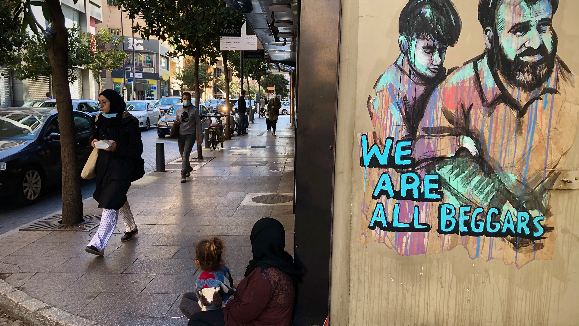 Libanon, Beirut: Menschen gehen an einer Frau vorbei, die mit ihrer Tochter auf dem Boden sitzt und bettelt, neben ihr ein Grafitto mit dem Text: "We are all beggars". | dpa