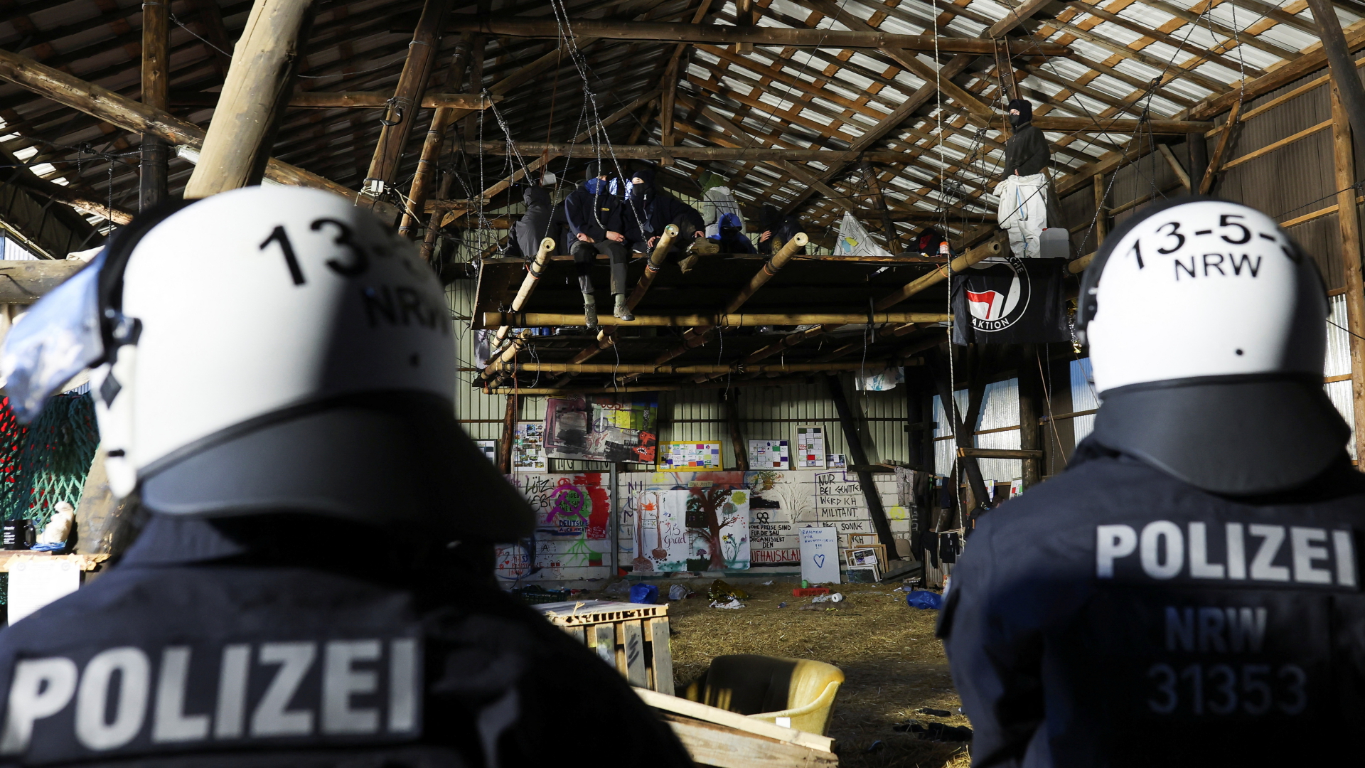 Polizisten bewachen Aktivisten, die sich in einer Halle auf einer hängenden Holzkonstruktion verschanzt haben.  | REUTERS