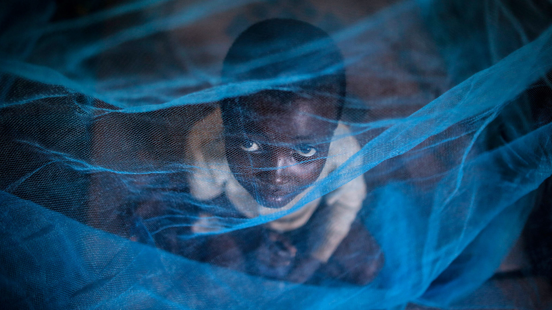Ein Flüchtlingskind aus Burundi sitzt unter einem Moskitonetz gegen Malaria. | dpa