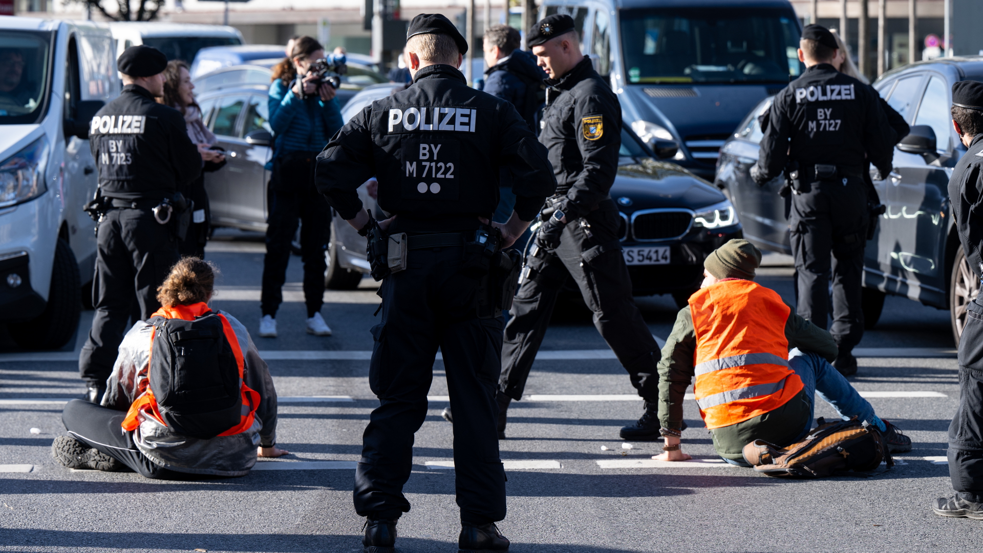 Polizeibeamte stehen neben Klimaaktivisten, die sich in München auf die Fahrbahn geklebt haben. | dpa