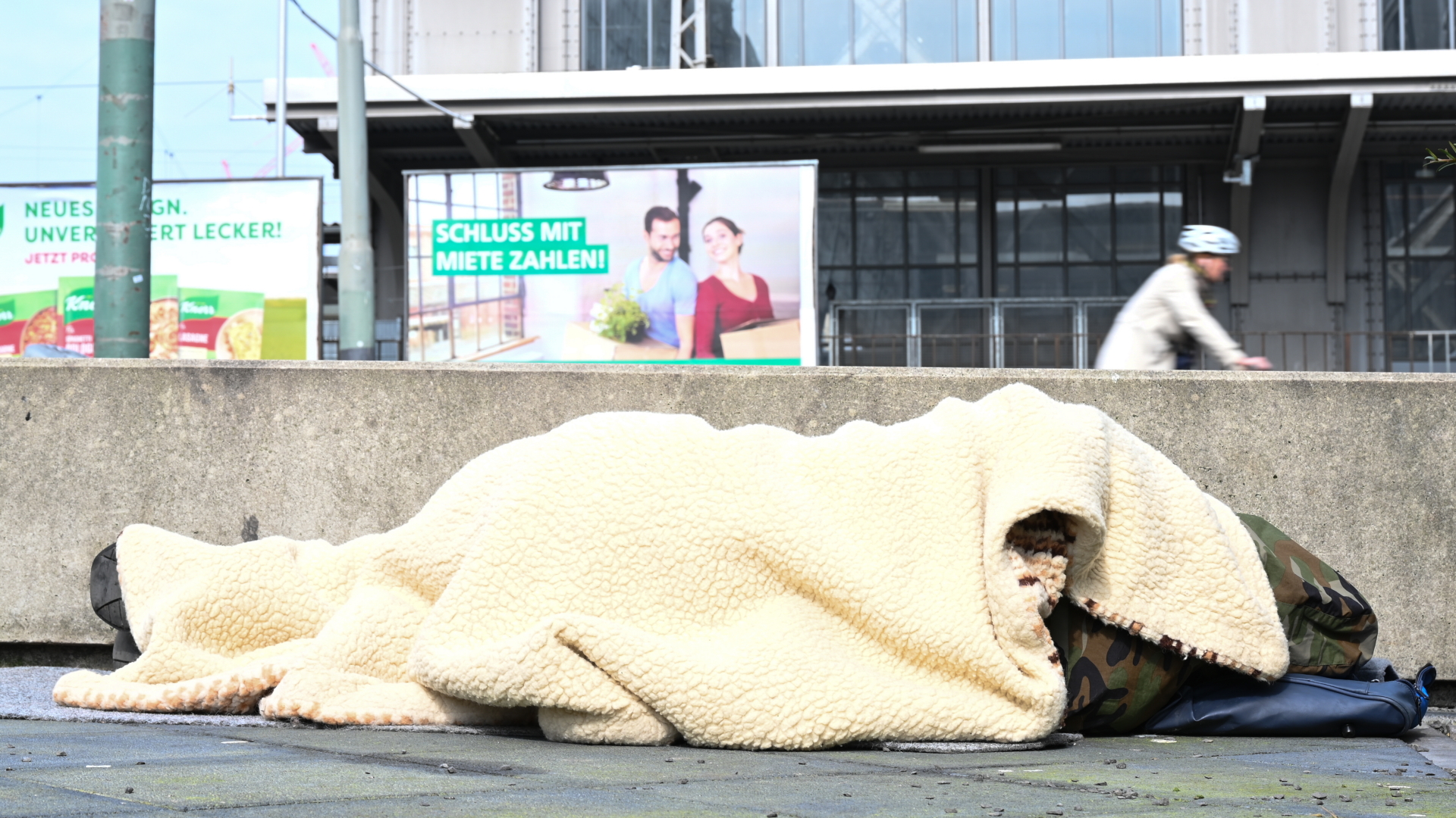 Ein Obdachloser schläft hinter einer Betonmauer am Hauptbahnhof von Frankfurt/Main. (Archivbild) | dpa