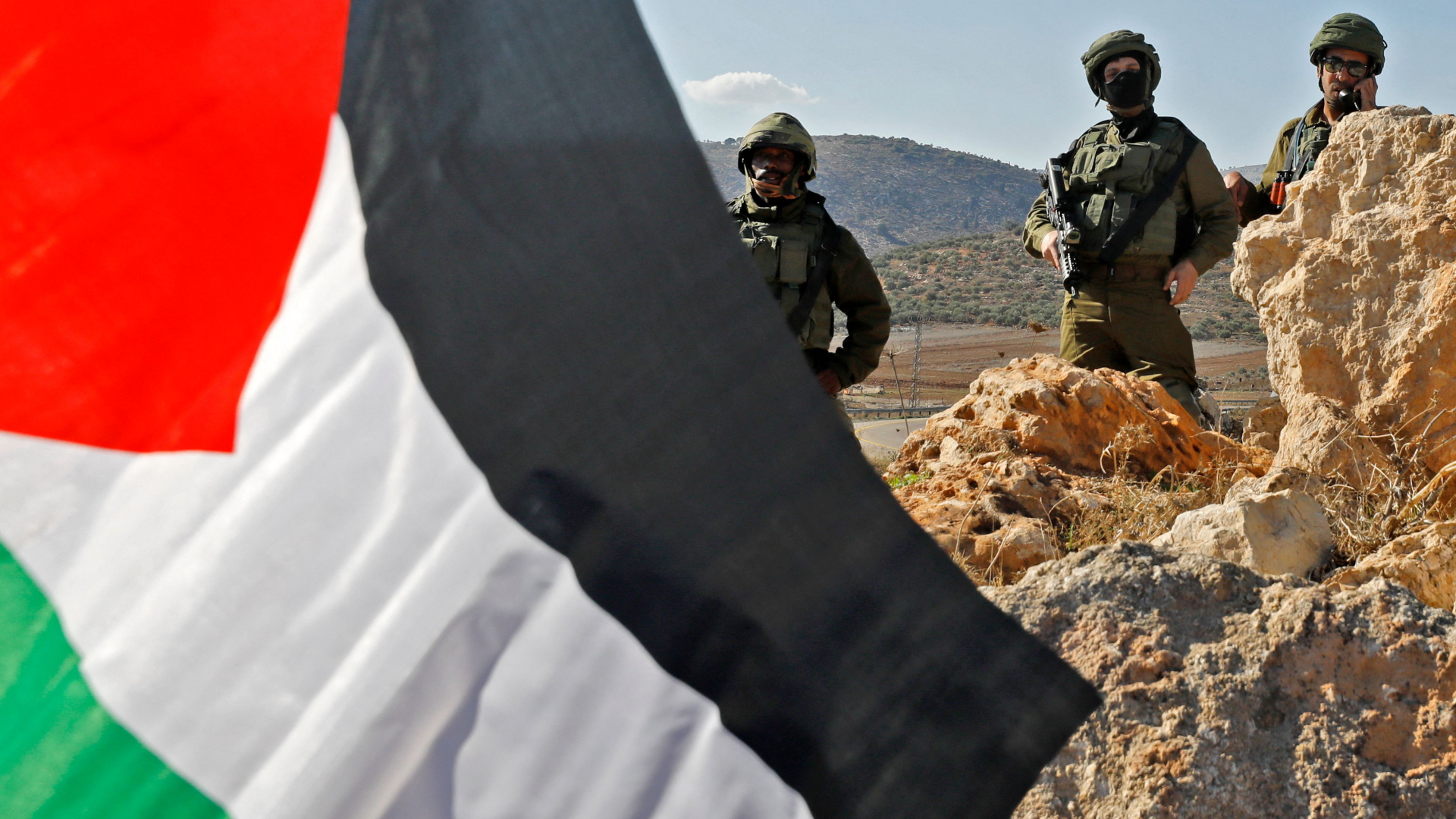 Israelische Soldaten stehen im Westjordanland hinter einer von Palästinensern geschwenkten Fahne | AFP